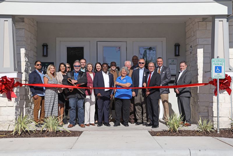 People about to cut a big red ribbon at an apartment clubhouse