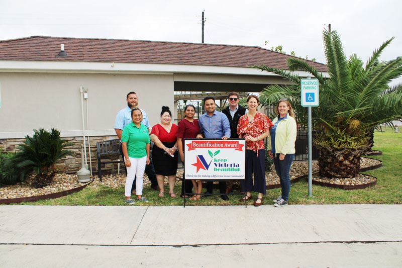 Group photo with KVB sign in front of a pool clubhouse with short palm trees and landscaping.