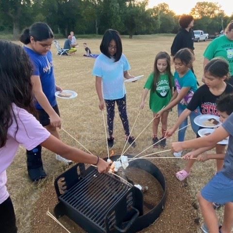 Kids roast marshmallows around a fire