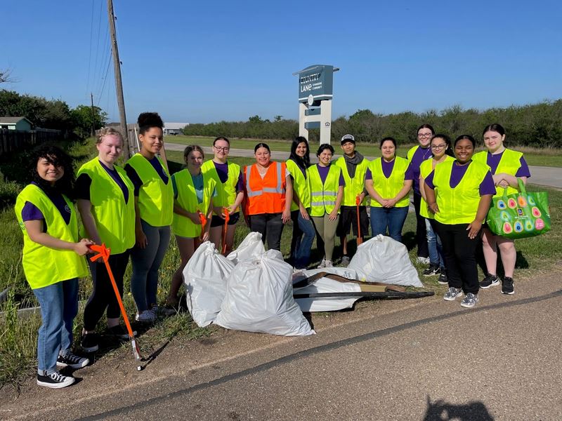 Large group of people near Country Lane sign with safety vests, grabbers and filled trash bags