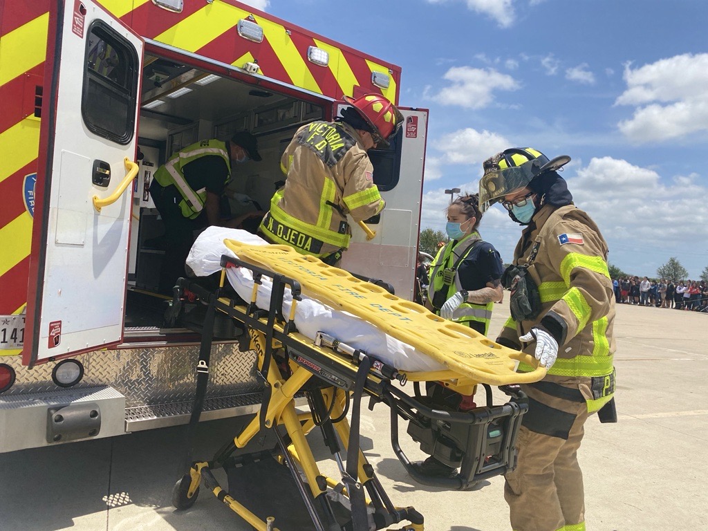 Two uniformed firefighters at a training facility with an ambulance in the background
