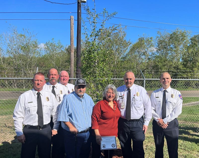 Group photo in front of a young tree. Five in fire department dress clothes, two in casual clothes