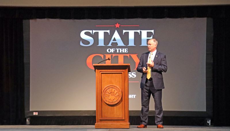 Mayor Jeff Bauknight stands near a podium with a State of the City backdrop