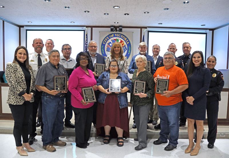 Large group photo in Council chambers. Nine people hold plaques; a few wear Police or Fire uniforms