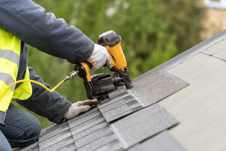 Close up of someone using a power tool to install shingles on a roof