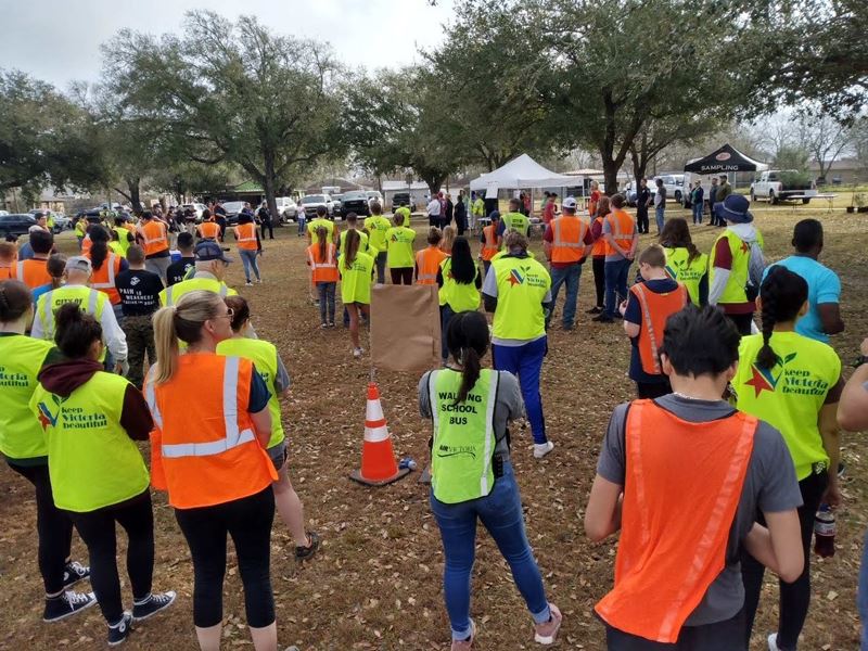 Large group of people in yellow and orange safety vests in a park