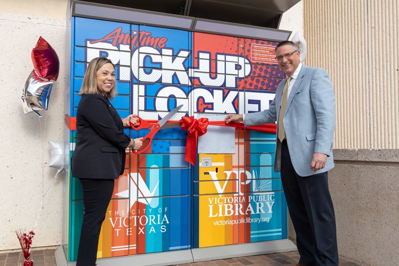 Jessica Berger uses scissors to cut a red ribbon on the locker while Duane Crocker holds the ribbon