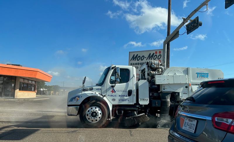 A street sweeper with City logo kicks up dust near Moo Moos