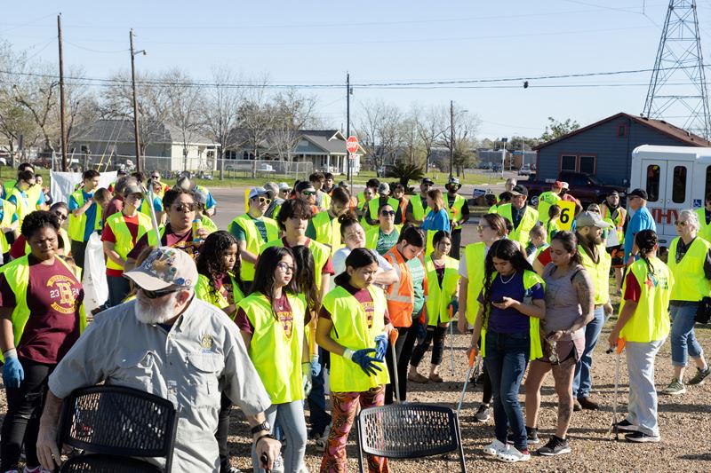 Large group of people in a parking lot, many wearing work vests