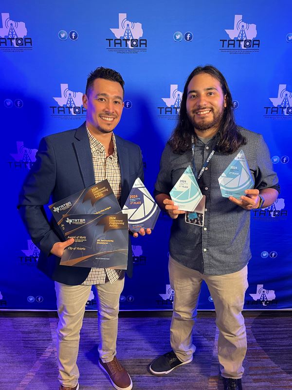 Two men holding five awards in front of a TATOA backdrop