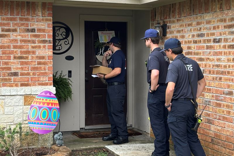 Three firefighters stand at the door of a home that is decorated for Easter.