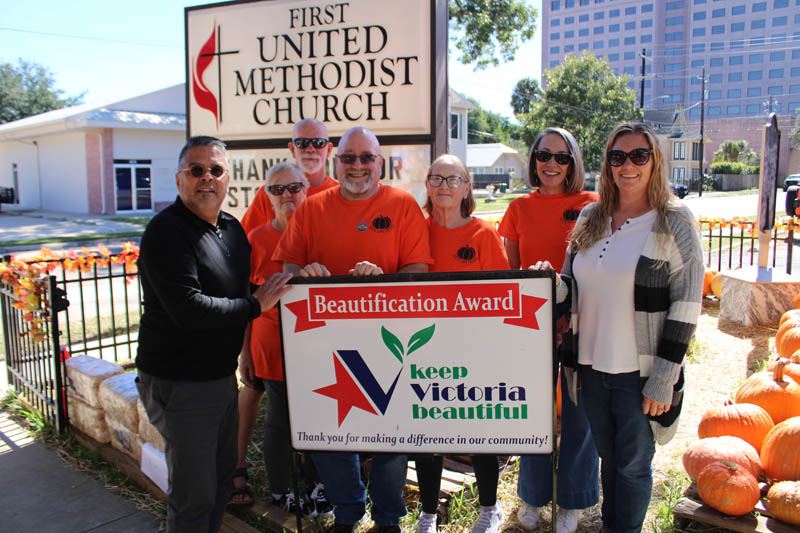 Group photo, most wearing orange, with KVB sign at a pumpkin patch by a Methodist Church sign.