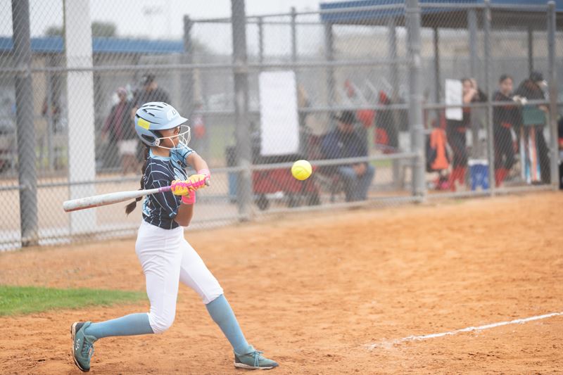 A young softball player holds her bat ready to hit a ball that is coming toward her