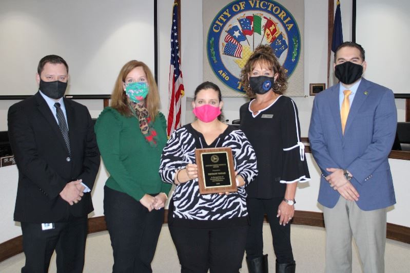 Five people pose for a group photo. The woman in the center holds a plaque.
