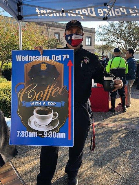 A police officer holds a cup of coffee and a sign advertising the Coffee with a Cop event
