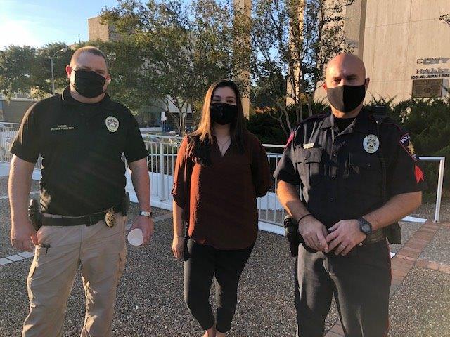 Two police officers pose for a photo with a woman at the City Hall courtyard.