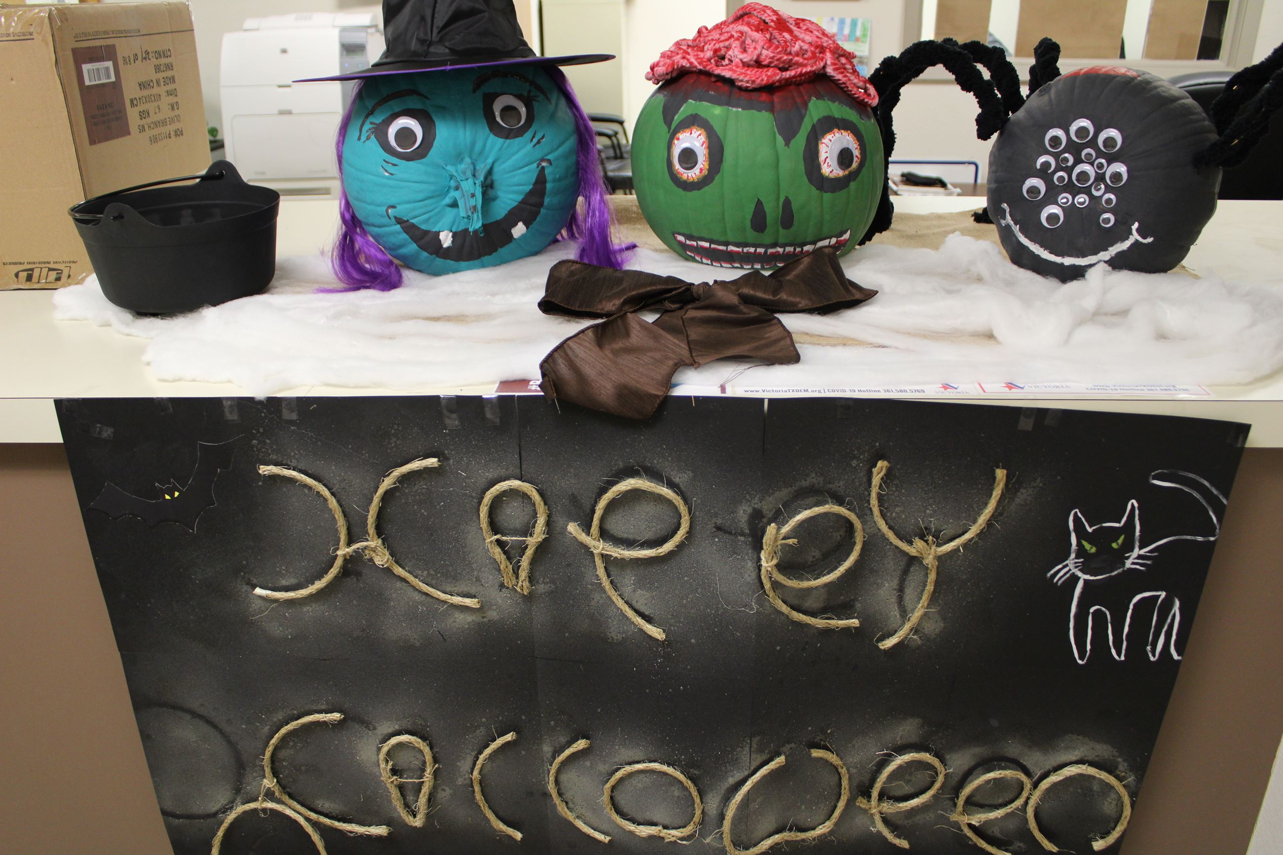 Pumpkins decorated as witch, zombie and spider. Sign reads 