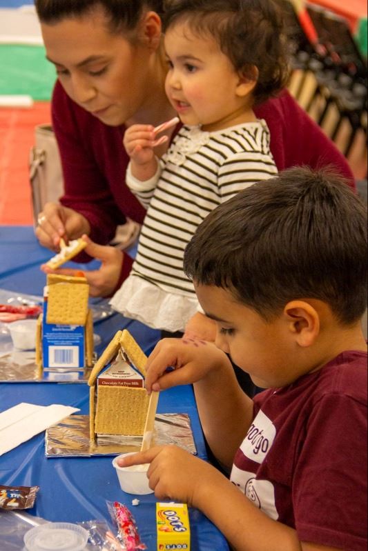 A woman and two children build gingerbread houses from graham crackers, milk cartons and candy.