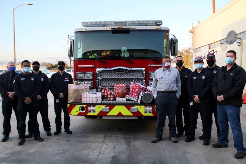Firefighters stand in front of parked fire engine with wrapped gifts arranged across the front.
