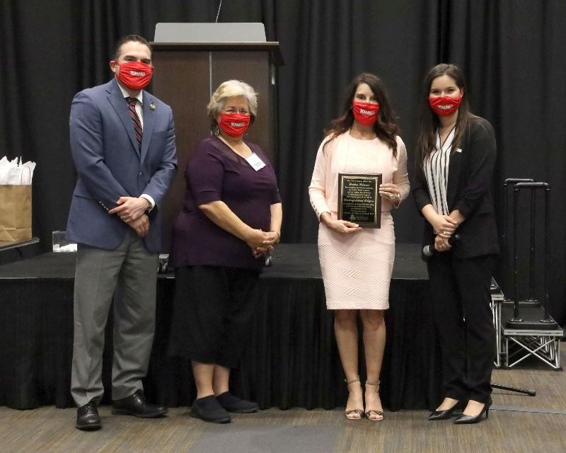 Woman holding plaque poses with three other people.