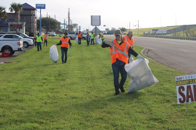 People in orange and yellow safety vests walk along loop near IHOP with trash bags collecting trash