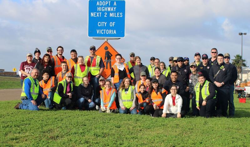 Group of volunteers posing for picture in front of Adopt A Highway blue sign