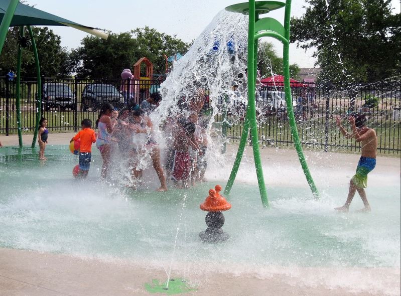 Young kids stand under a water pouring feature at a splash pad