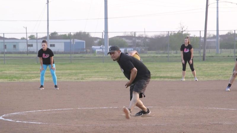 A man prepares to throw a kickball. Two female players stand in the background.