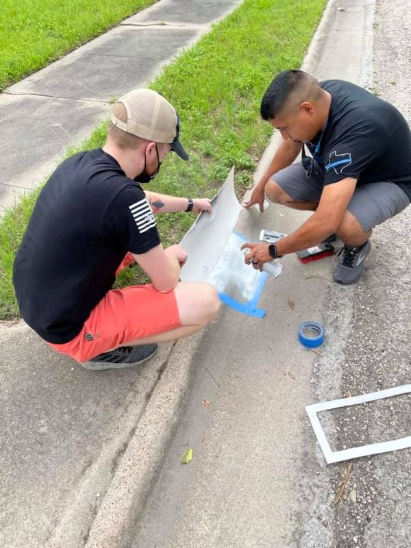 Two people squat near curb and use spray paint and stencils to paint address numbers
