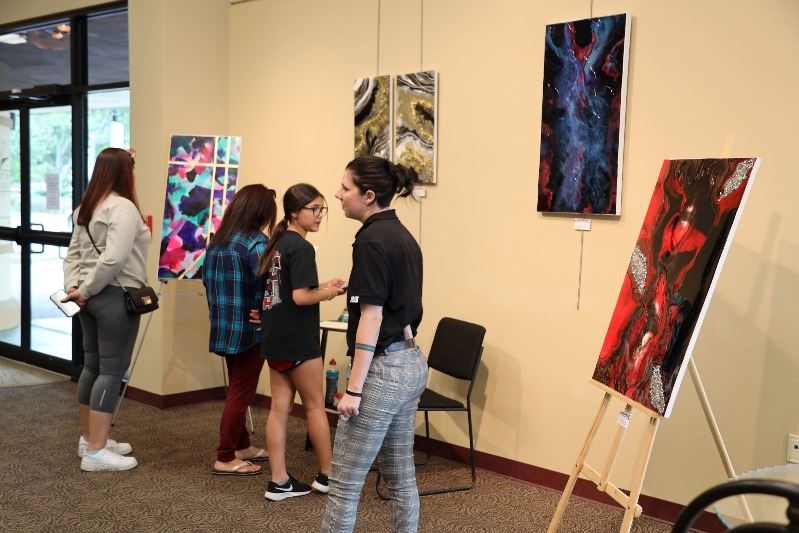 Four people look at colorful paintings on easels and wall at Leo J. Welder Center.