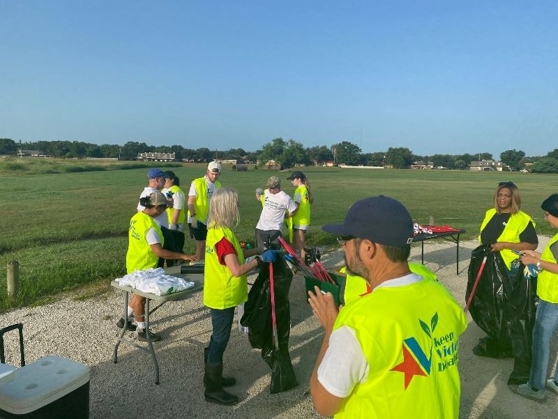 People in yellow safety vests in a parking lot gather trash grabbers and other supplies
