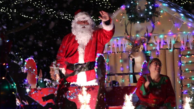 Santa and elves wave from lighted parade float