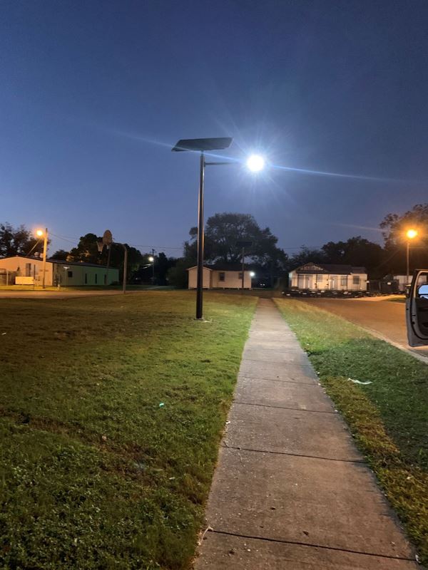 An LED street light shines brightly at night by a sidewalk.