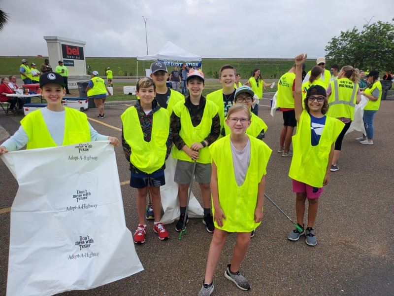 Group of kids wearing safety vests. One holds a Don't Mess with Texas bag.