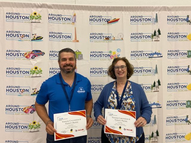 Two people holding certificates in front of an Around Houston backdrop