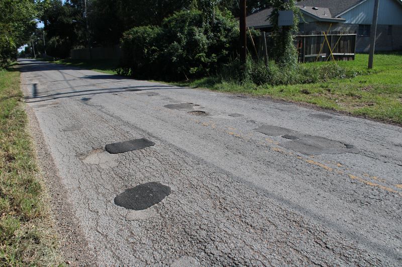 A rough street with several discolored patches and potholes