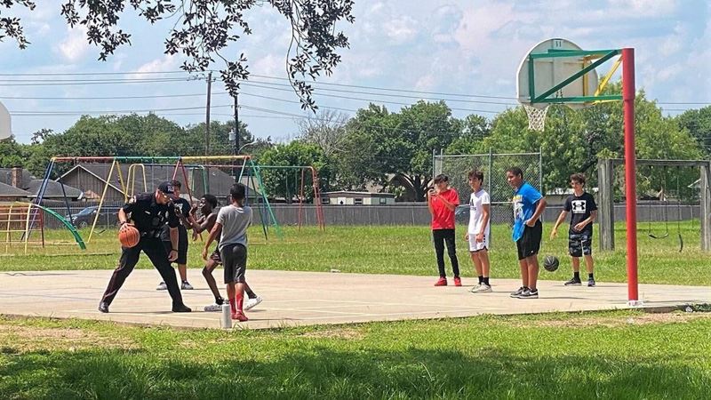 A uniformed police officer plays basketball with a group of young people