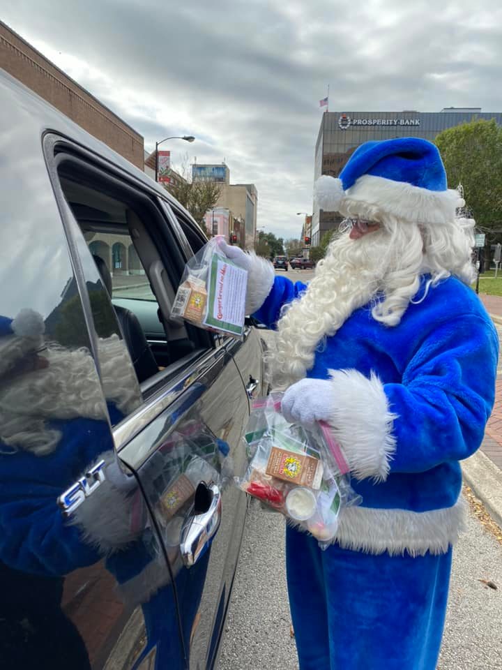 Blue Santa hands plastic bags through a car window with frosting, candy and other items