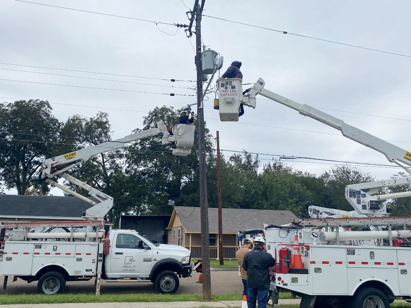 Two men in truck lift buckets fix street lights while two people near a truck assist