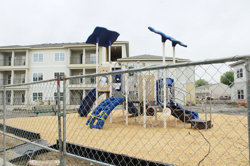 A new playground in a fenced-off area at an apartment complex, with caution tape on one ladder.
