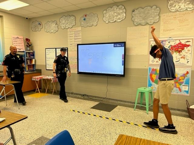 Two police officers watch as a student wearing drunk goggles attempts to walk along a marked line.