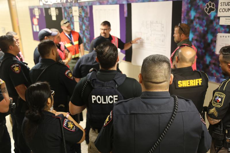 Victoria Police Department and Victoria Sheriff's Office personnel stand in a hallway at a school Opens in new window