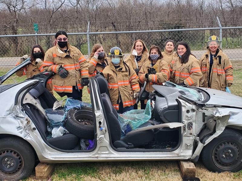 Group of people stand around a wrecked car with the roof and doors taken off