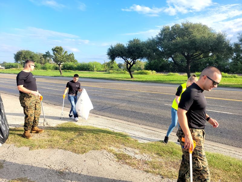 People with trash bags and grabbers walk along the side of a roadway