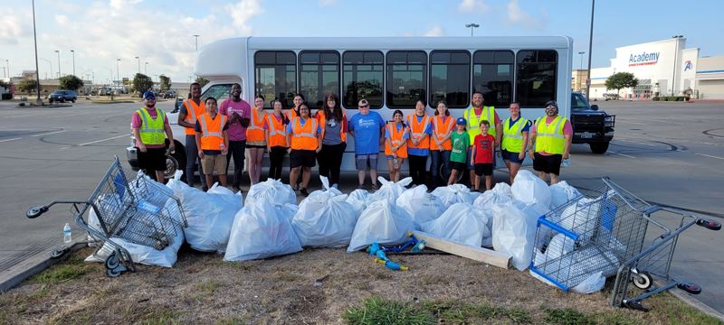 A group of people pose with collected trash bags and two discarded shopping carts