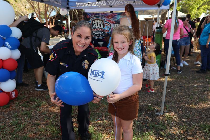 A uniformed police officer and a young girl holding balloons outside Opens in new window