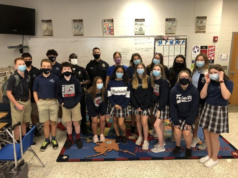 About 14 uniformed eighth-grade students pose for a photo with two men and one woman in the back.