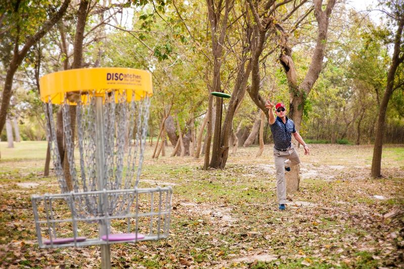 Man tosses disc golf disc into nearby basket at Riverside Park.