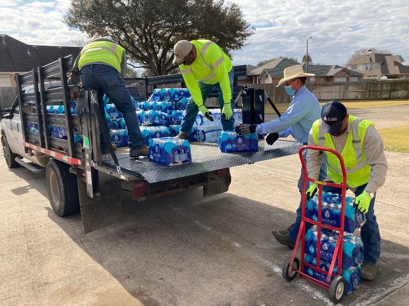 Workers unload cases of bottled water from a truck and place them on a dolly.