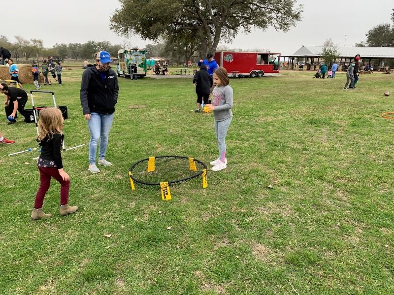 Two young girls play a game with a plastic ball and a bouncy net placed near the ground. 